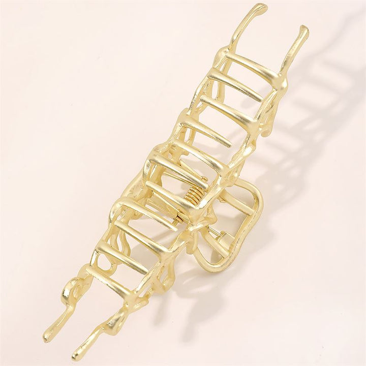 Die SOHO Asli Metal Hair Claw – Silver von SOHO zeichnet sich durch ein geometrisches, leiterartiges Design aus. Vor einem hellen Hintergrund präsentiert, hebt dieses elegante Accessoire seine federnde und gezackte Metallstruktur hervor.