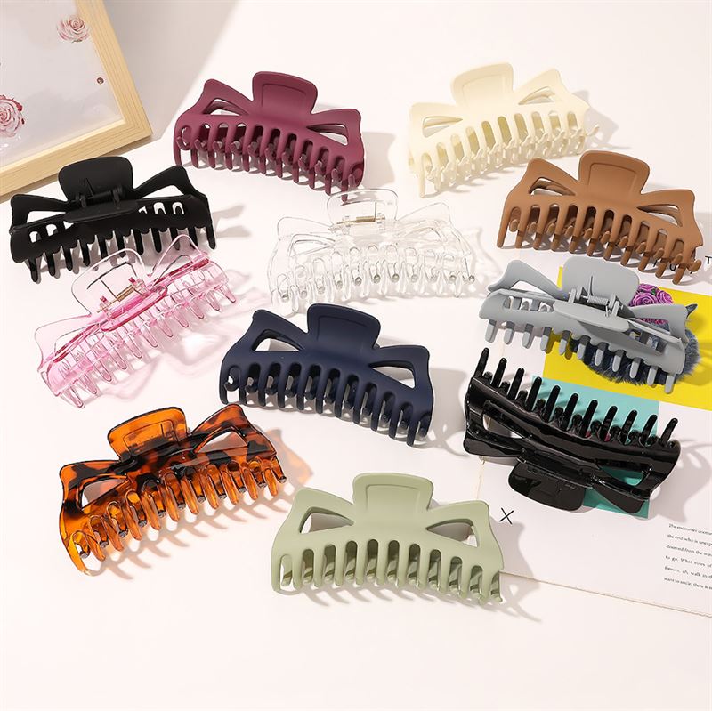 The SOHO Astrid Hair Claw in Navy by SOHO is a large clip ideal for thick hair, offering a secure hold. The navy color looks elegant, and the claw is displayed neatly on a white surface next to papers and a picture frame.