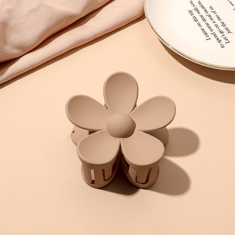 The SOHO Bloom Hair Claw - Brown by SOHO, featuring five petals, sits on a light beige surface next to a white plate with text and folded fabric.