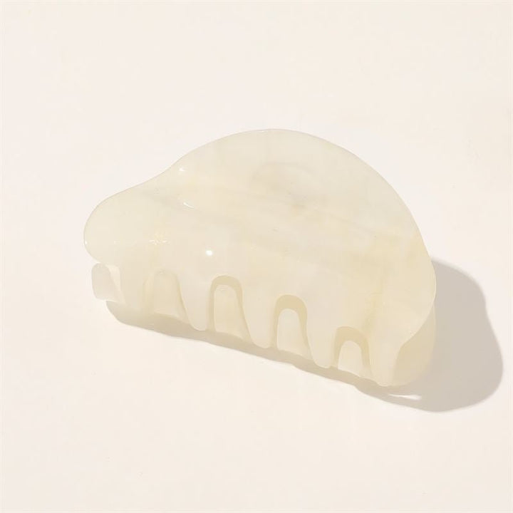The SOHO Cleo Hair Claw - White by SOHO is a translucent, off-white marble medium hair clip with a curved design and wide teeth, elegantly displayed on a plain light background.