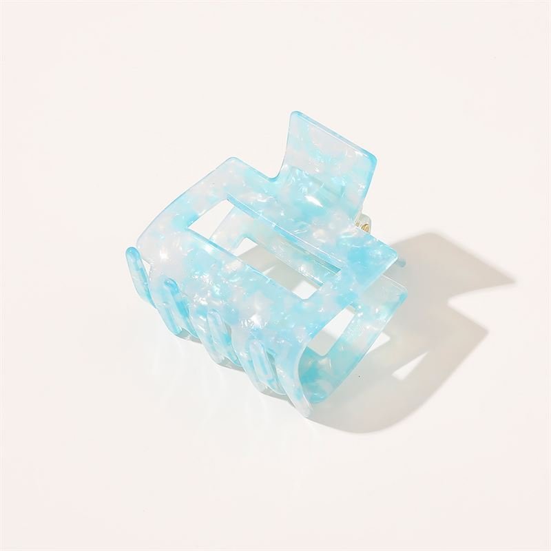 Die SOHO Ema Hair Claw in Crystal Blue von SOHO zeichnet sich durch ein durchscheinendes blaues Marmormuster aus, das auf weißem Hintergrund mit einem weichen Schatten dargestellt wird – ein schickes Accessoire, ideal für elegante Frisuren.