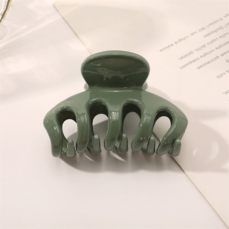 Die SOHO Esta Hair Claw – Green von SOHO verfügt über gebogene Zinken für zusätzlichen Halt und wird auf einer weißen Oberfläche neben einem teilweise sichtbaren Blatt bedrucktem Papier gezeigt.