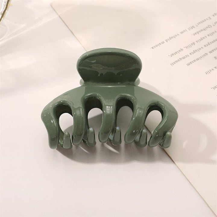 Die SOHO Esta Hair Claw – Green von SOHO verfügt über gebogene Zinken für zusätzlichen Halt und wird auf einer weißen Oberfläche neben einem teilweise sichtbaren Blatt bedrucktem Papier gezeigt.