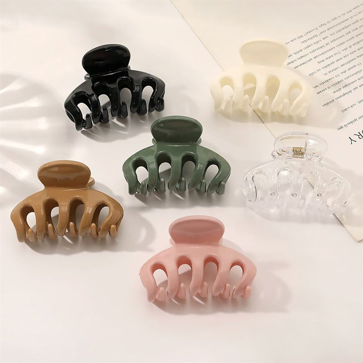 Die SOHO Esta Hair Claw in Grün von SOHO wird auf einer weißen Fläche neben einem aufgeschlagenen Buch gezeigt – ideal für zuverlässigen Halt und stilvolles Haarstyling.