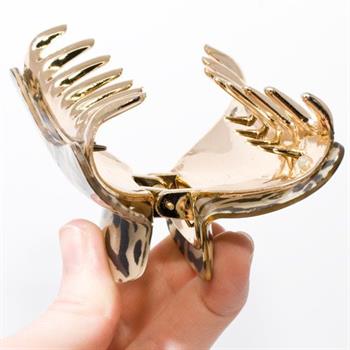 A hand holds the SOHO Hair Claw - Leopard by SOHO, a shiny gold-toned acrylic clip featuring a bold leopard motif.
