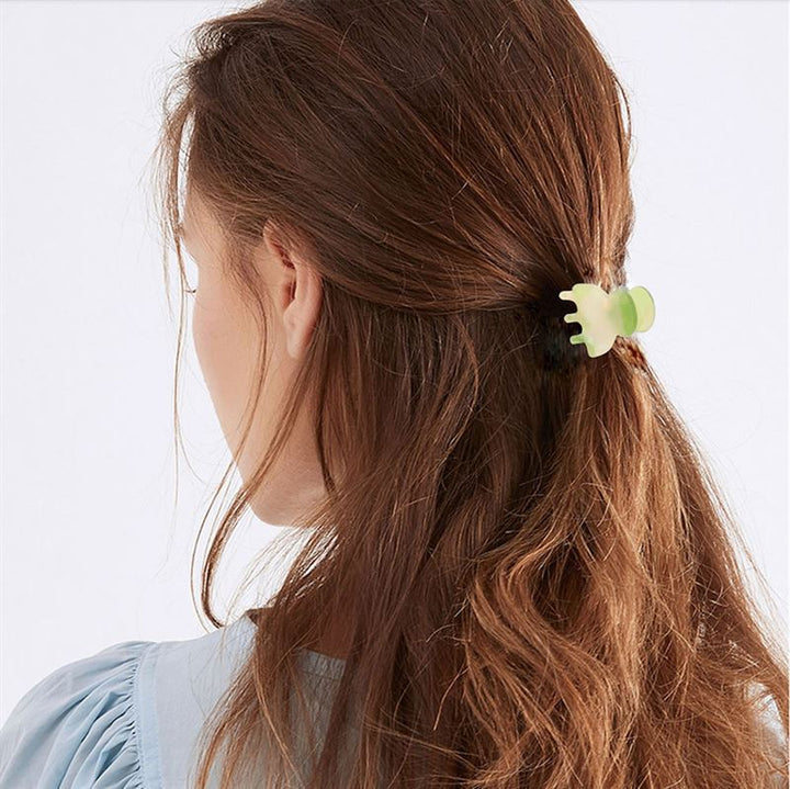 A woman with long brown hair, partially tied back with the SOHO Hara Mini Hair Claw - Beach for a secure hold, is seen from behind wearing a light blue top.
