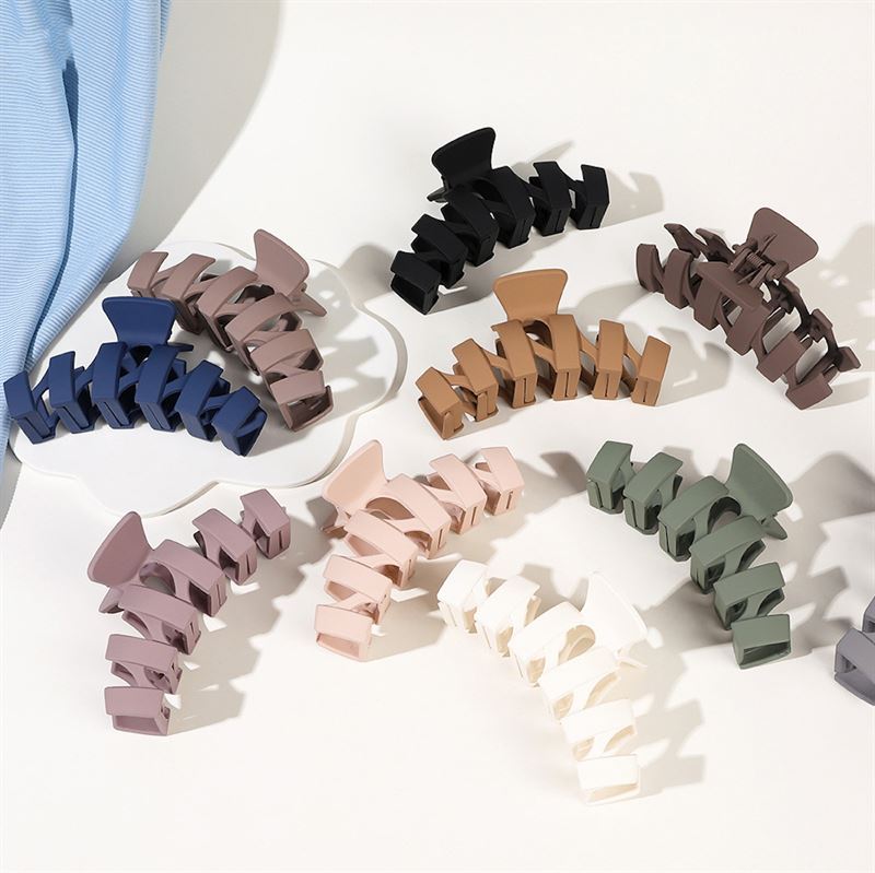 The SOHO Just Hair Claw in black, along with other SOHO matte-finish clips in blue, beige, brown, green, and white, are displayed in a semi-circle on a white surface.