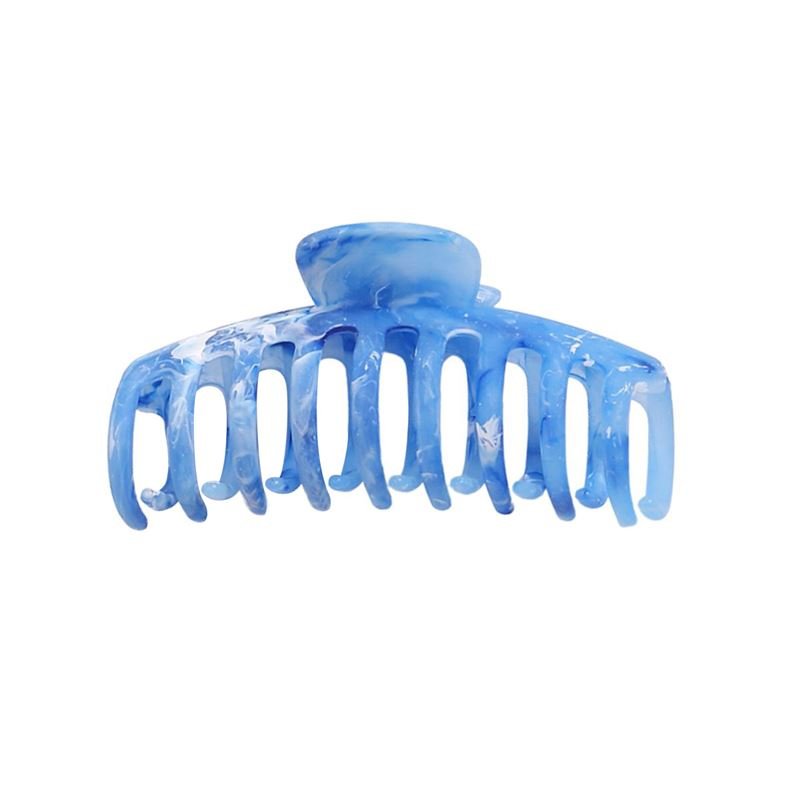 The SOHO Kana Marble Hair Claw - Ocean by SOHO features wide, curved teeth and a rounded hinge for a strong grip. This stylish blue marble hair accessory is shown isolated on a white background.