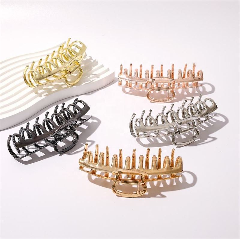 Five SOHO Kana Metal Hair Claws by SOHO in gold, silver, rose gold, black, and light gold titanium rest on a white wavy surface. These large clips offer strong grip for all hair types and add chic style to any look.
