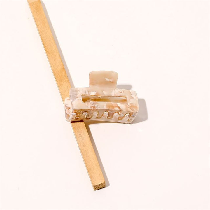 The SOHO Leia Mini Hair Claw in Beige Marble rests on a light wooden stick, positioned diagonally against a plain white background—an elegant accessory for effortless hairstyling.