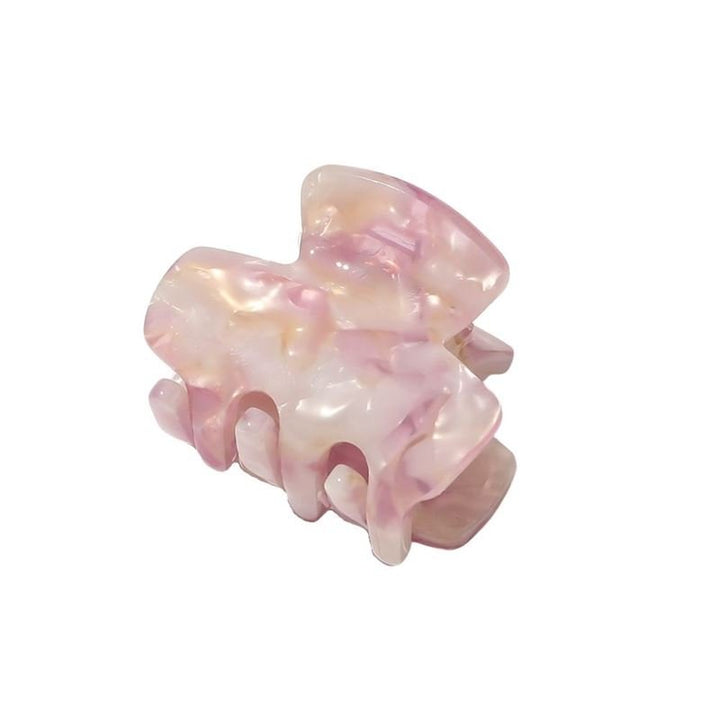 The SOHO Loa Mini Hair Claw - Blush by SOHO features a blush pink marbled design, glossy finish, curved prongs, and a rectangular shape—perfect as a small hair claw for everyday elegance.