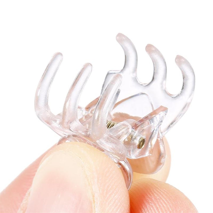 A close-up of fingers holding a SOHO Lucca Mini Hair Claw—transparent, with four prongs and a metal spring hinge—perfect for fans of SOHO’s mini hair accessories.