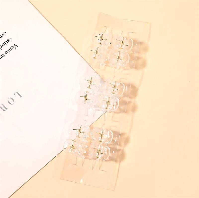 Two pairs of clear earrings with gold studs are arranged on a peach surface next to a white sheet with printed text, alongside SOHO Lucca Mini Hair Claws - Transparent by SOHO.