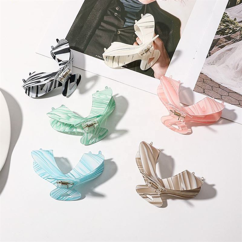 Die SOHO Malou Hair Claw – Green von SOHO wird auf einer weißen Fläche neben einem aufgeschlagenen Modemagazin präsentiert und zeichnet sich durch ihre Schmetterlingsform und ihr stilvolles Pastell- und Streifendesign aus.