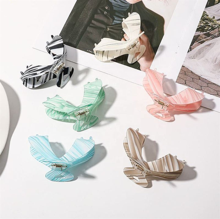 Die SOHO Malou Hair Claw – Green von SOHO wird auf einer weißen Fläche neben einem aufgeschlagenen Modemagazin präsentiert und zeichnet sich durch ihre Schmetterlingsform und ihr stilvolles Pastell- und Streifendesign aus.