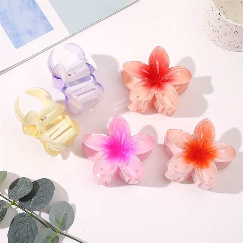Five SOHO hair clips are arranged on a white surface. Three are flower-shaped, including the SOHO Moana Hair Claw in yellow, in pink and orange, while the others feature butterfly and leaf shapes in pastel yellow and purple.