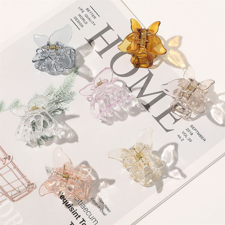 Die SOHO Naja Hair Claw in Espresso von SOHO wird als stilvolles Haaraccessoire auf einem aufgeschlagenen Magazin mit grünen Blättern und sichtbarem Hintergrundtext präsentiert.