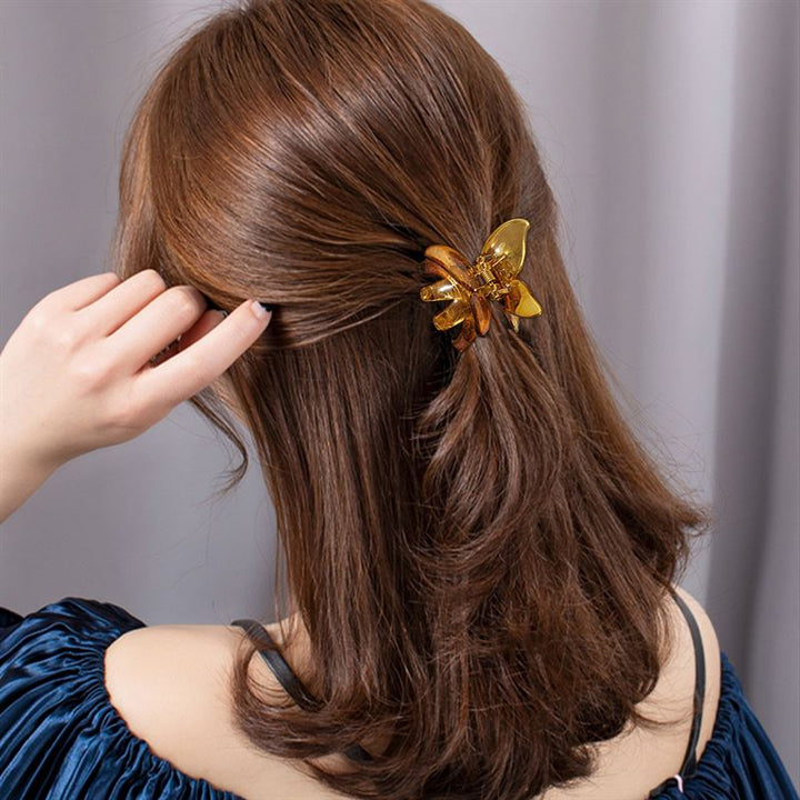 Eine Person mit mittellangem, transparentem braunem Haar trägt die SOHO Naja Hair Claw – Espresso von SOHO und hat einen Teil ihres Haares nach hinten gekämmt. Von hinten gesehen, in einem dunklen, schulterfreien Oberteil, hebt sie eine Hand in die Nähe ihres Kopfes und präsentiert dieses schicke Accessoire.