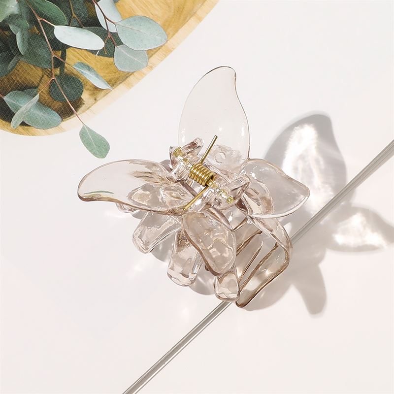 Die SOHO Naja Hair Claw – Espresso von SOHO mit durchscheinendem braunen Finish und goldener Feder ruht auf einer weißen Oberfläche mit grünen Eukalyptusblättern im Hintergrund, die dieses elegante Haaraccessoire ergänzen.