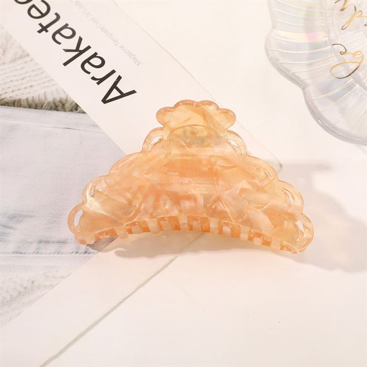 Die SOHO Naomi Hair Claw – Sunshine von SOHO ist ein pfirsichfarbenes, durchscheinendes Haaraccessoire mit gewelltem Rand, das auf einer weißen Fläche neben Papieren und einer weiteren durchsichtigen Klammer abgebildet ist – ideal, um jeder Frisur Eleganz zu verleihen.
