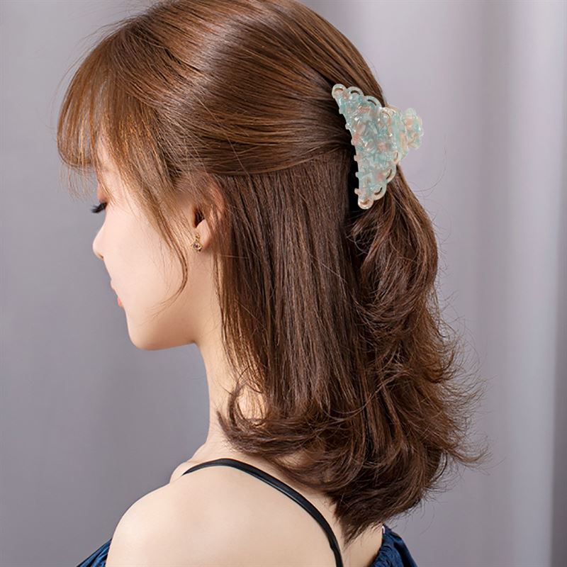 Eine Frau mit schulterlangen braunen Haaren, die elegant mit der SOHO Naomi Hair Claw – Sunshine gestylt sind, ist von hinten und von der Seite zu sehen. Sie trägt ein dunkles, ärmelloses Oberteil und kleine Ohrringe vor einem neutralen Hintergrund.
