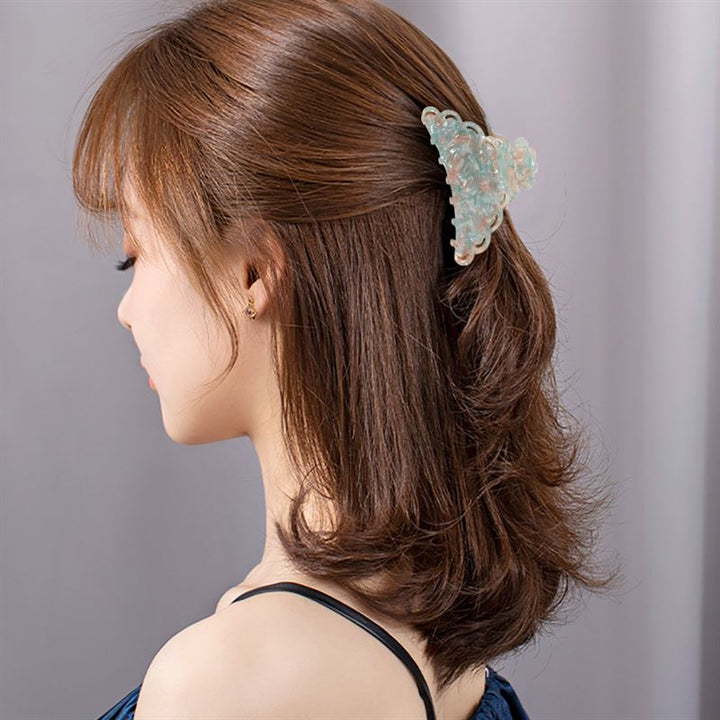 Eine Frau mit schulterlangen braunen Haaren, die elegant mit der SOHO Naomi Hair Claw – Sunshine gestylt sind, ist von hinten und von der Seite zu sehen. Sie trägt ein dunkles, ärmelloses Oberteil und kleine Ohrringe vor einem neutralen Hintergrund.