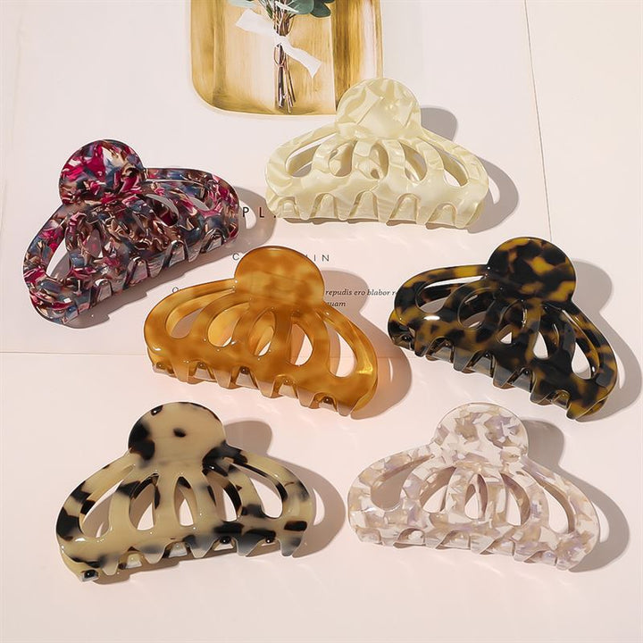 Six SOHO Olivia Hair Claw clips in assorted marble patterns are displayed on a white surface with a magazine underneath—these SOHO hair accessories add stylish flair to any look.