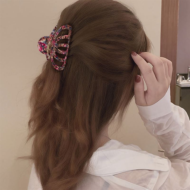 A person with long brown hair, styled half up and secured with the SOHO Olivia Hair Claw - Marble, is shown from behind in a white top, touching their hair and showcasing this vibrant SOHO accessory.