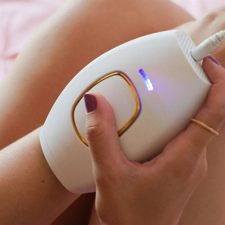 A person with painted nails uses the UNIQ IPL Hair Removal Device—featuring a glowing blue indicator—for smooth, pain-free, permanent hair reduction at home.