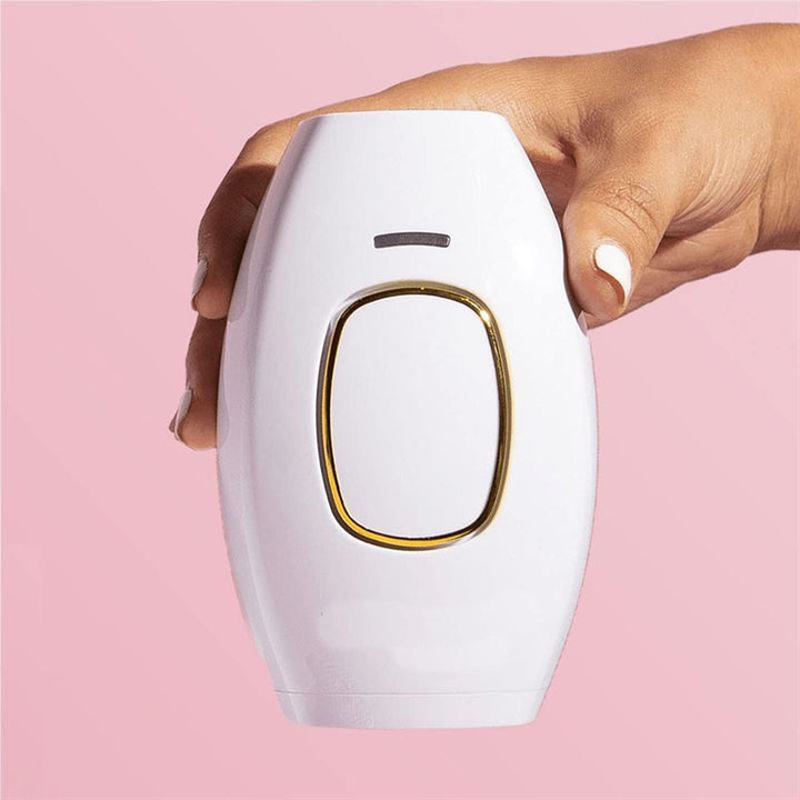 A hand with white-painted nails holds the UNIQ IPL Hair Removal Device (600,000 flashes) against a pink background—smooth, pain-free, permanent hair reduction at home by UNIQ.