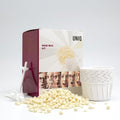 Das UNIQ Nose Wax Kit von UNIQ ermöglicht eine einfache Entfernung von Nasenhaaren mit weißen Wachskügelchen, Kunststoffapplikatoren, Papierbechern und einer lustigen Verpackung mit ausdrucksstarken Gesichtern und dem Text „Nose Wax Kit”.