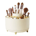 The UNIQ Rotating Makeup Organiser in Cream White features a tiered, ribbed design with compartments and gold legs, offering easy storage and organisation for brushes, lipsticks, pencils, and beauty products.